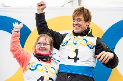 Two olympic athletes smiling on podium with gold medals. 