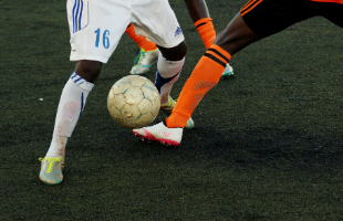 Two footballers tackling on grass pitch 