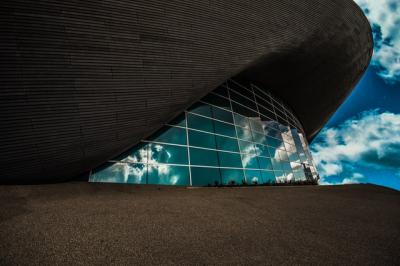 Image outside the side of a building with glass panels reflecting bright blue and cloudy sky. 