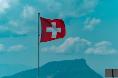 Swiss flag against bright blue cloudy sky. 