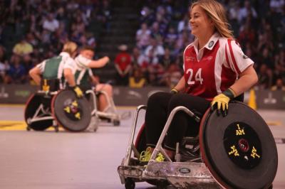 Wheelchair athletes on a court in front of crowded stadium. 