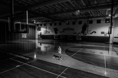 Black and white image of basketball player alone on a basketball court indoors.